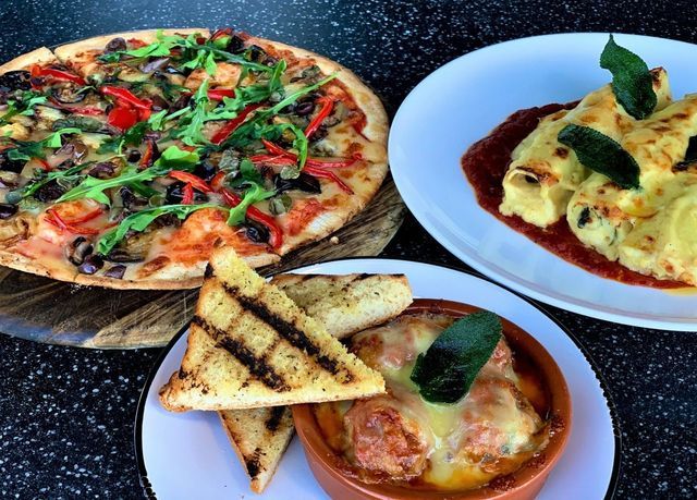 Pizza, baked pasta, and meatballs with garlic bread on a dark table.