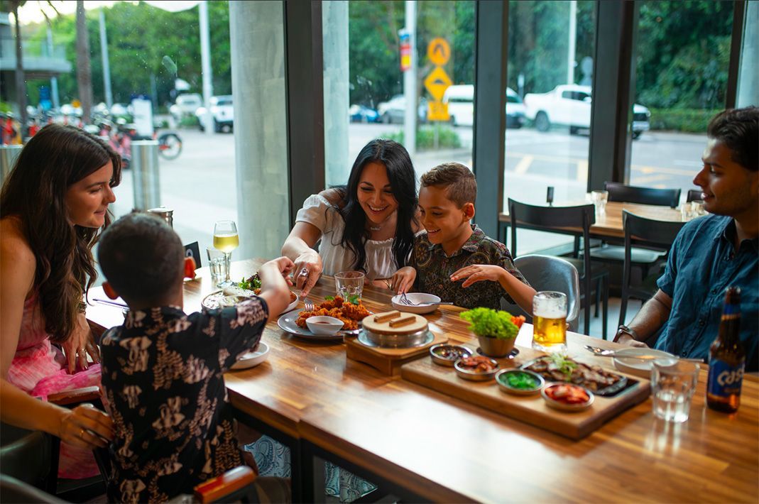 Family dining at a restaurant with various dishes on the wooden table, near a window.