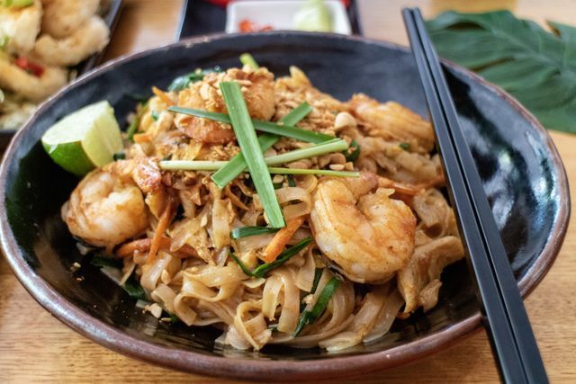 Pad Thai with shrimp, lime wedge, and chopsticks in a dark bowl.