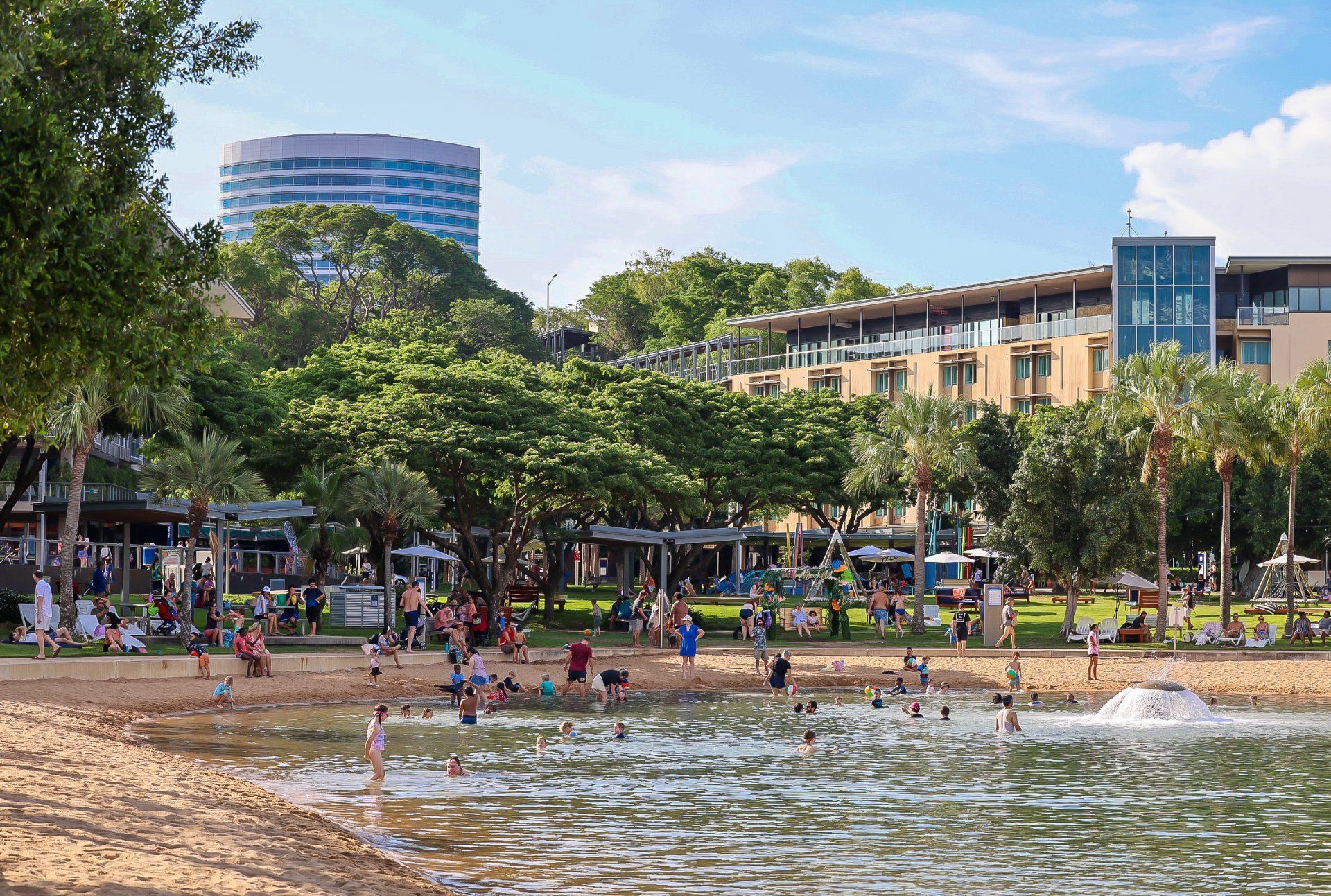 Woman stands in front of a watermelon wave mural. Pink background, black overalls, white sneakers.