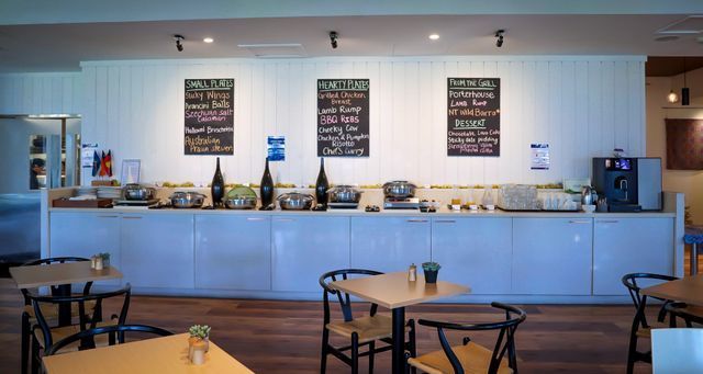 Buffet setup in a dining area. Long counter with food, three menu boards above. Tables and chairs in the foreground.
