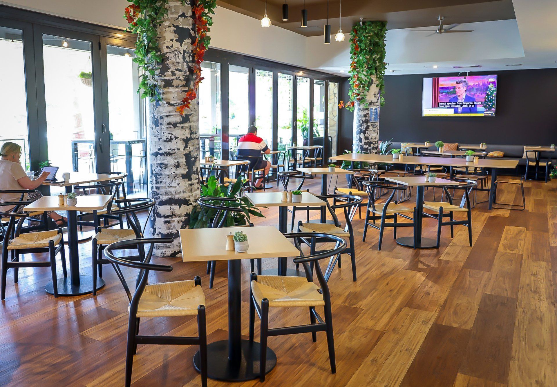 Interior of a cafe with tables and chairs, wood floors, and decorative birch columns.