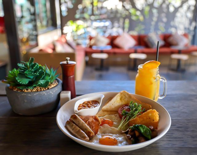 Breakfast plate with sausage, eggs, toast, hashbrown, and orange juice, served in a cafe.