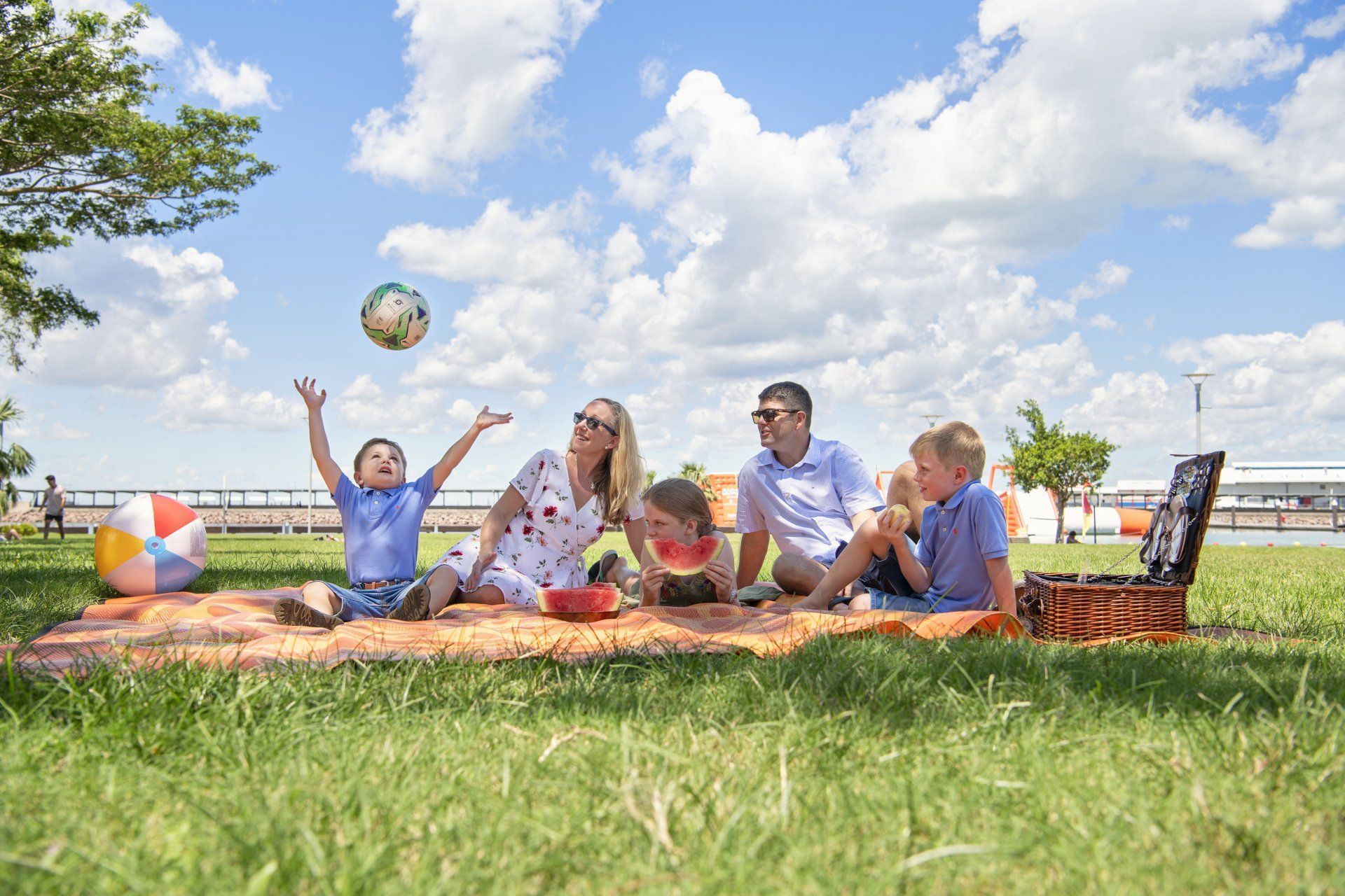 Family on a picnic in a park; a child is catching a ball, sunny day.
