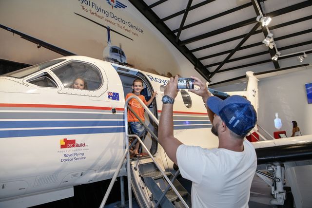 Man taking a photo of two people exiting a white airplane with blue and red stripes in a hangar.