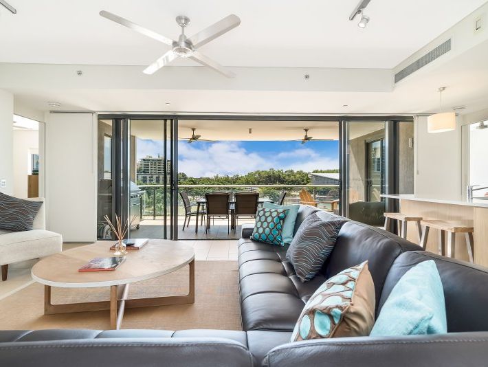 Living room with black leather sectional, open to a balcony with table and chairs.