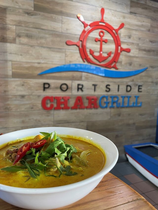 Bowl of soup in front of "Portside Char Grill" sign with red anchor symbol. Wooden background.