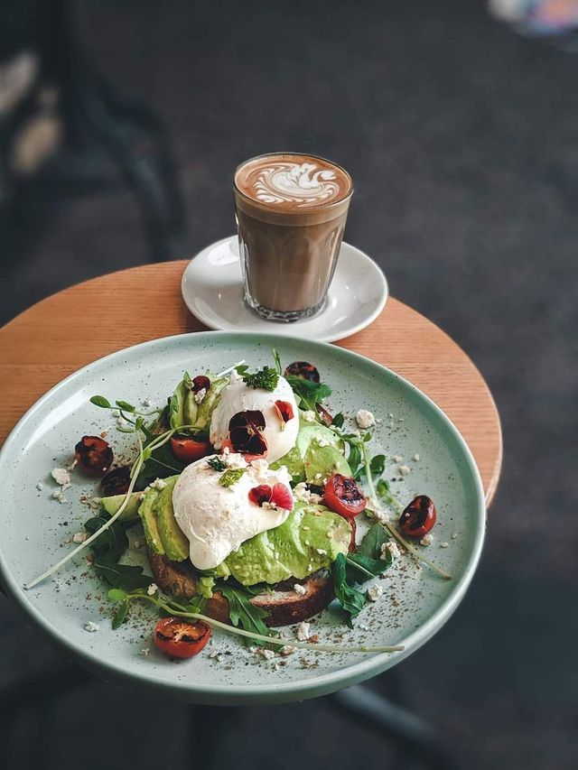 Avocado toast with poached eggs and coffee on a wooden table.