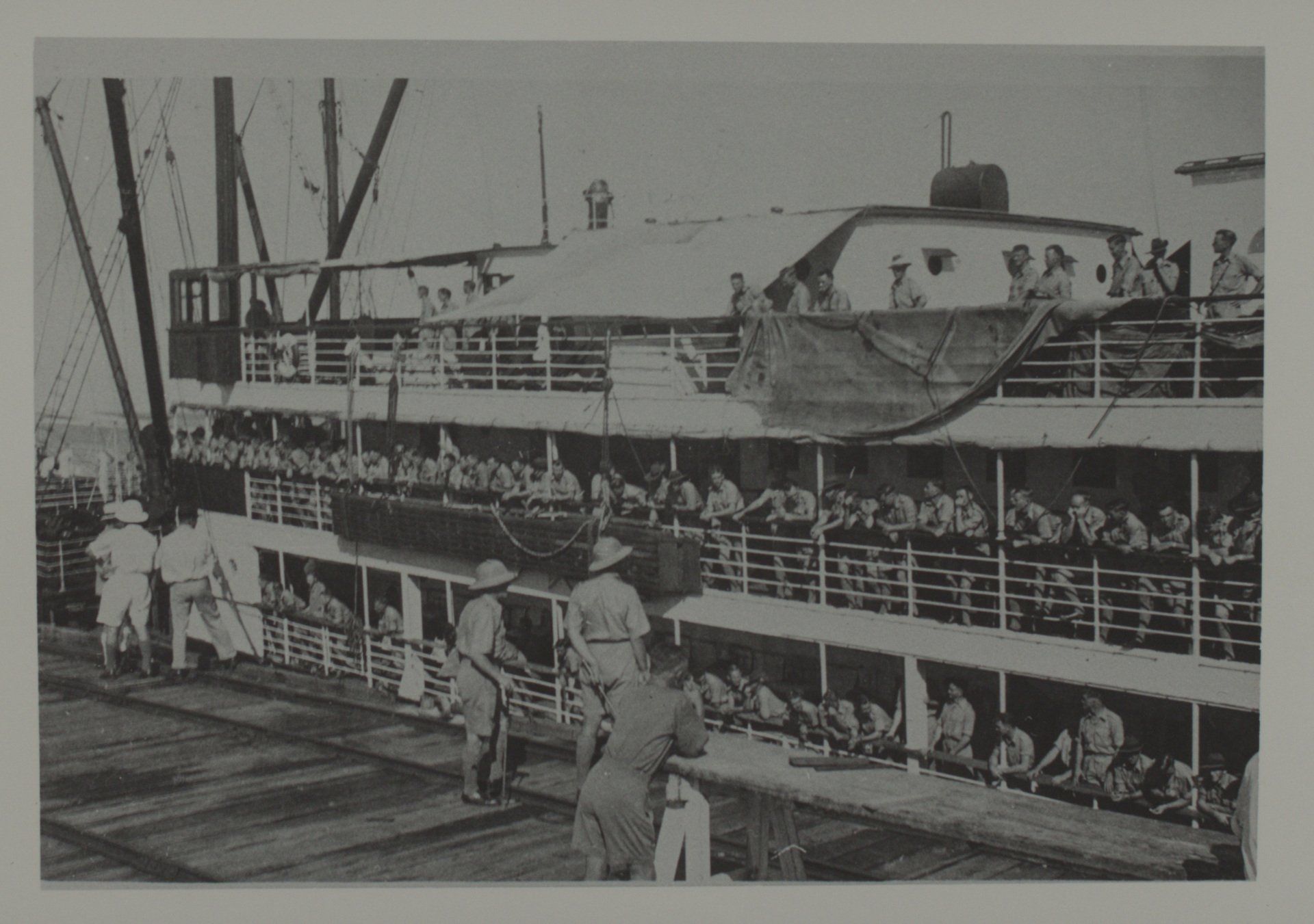 Soldiers on a multi-deck ship, likely during wartime, at a dock, facing the shore.