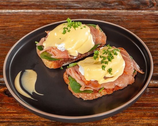 Eggs Benedict on toast with hollandaise sauce on a black plate.