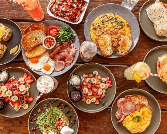 Overhead view of a wooden table covered with a variety of breakfast dishes and drinks.