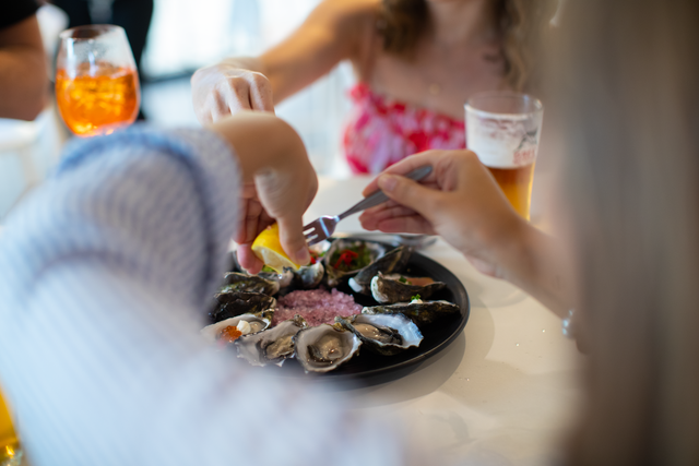 People eating oysters from a plate at a table, with drinks visible.