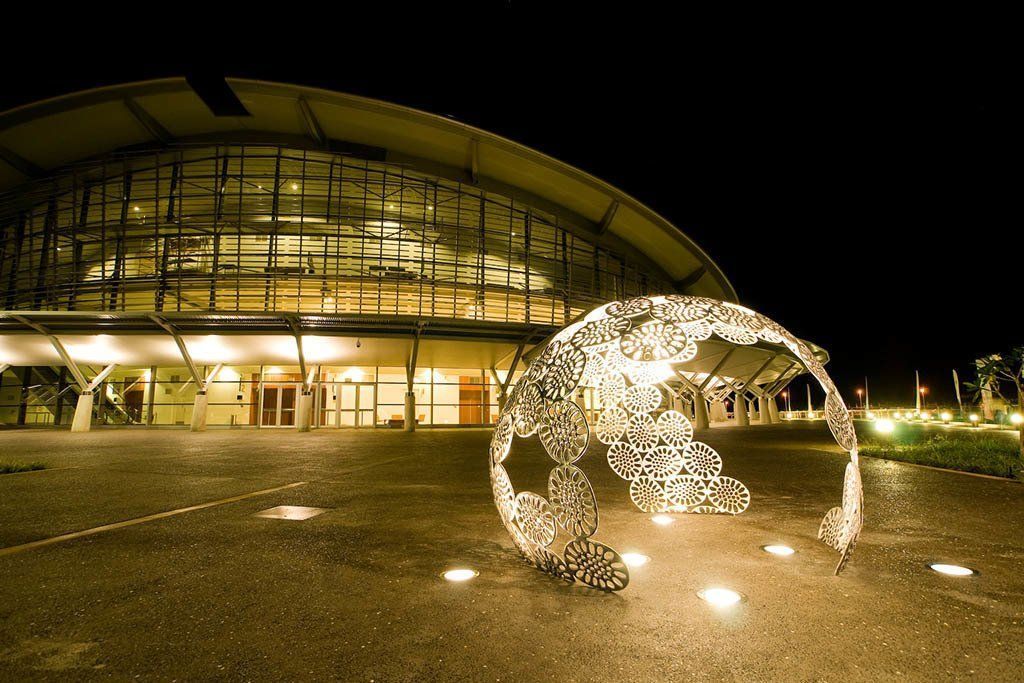 Night view of a modern building with a spherical sculpture and glowing ground lights.