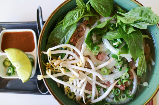 Bowl of Vietnamese pho with bean sprouts, herbs, and condiments.