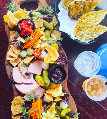 Charcuterie board with crackers, meats, cheeses, pickles, fruit, and grilled bread.