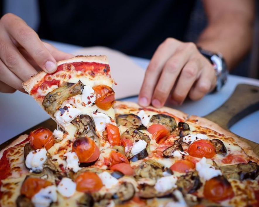 Person lifting slice of pizza with tomatoes, eggplant, and cheese.