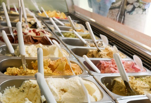 Gelato display case with various colorful flavors, each with a serving spoon.