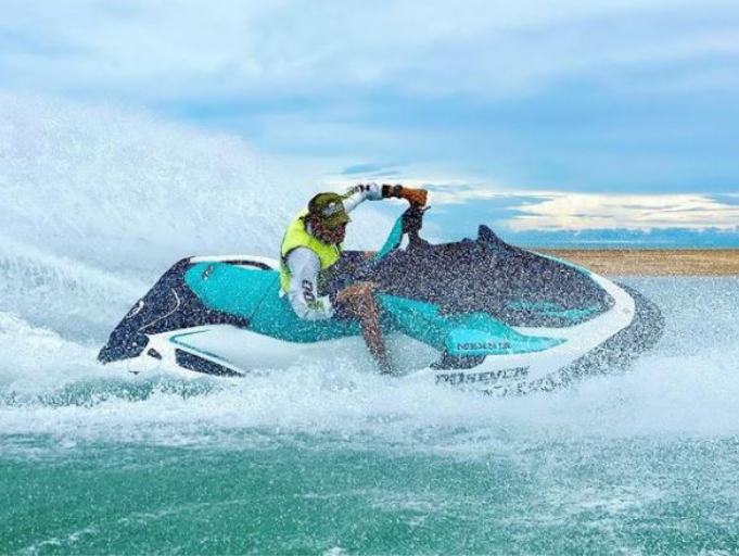 Person on a teal and black jet ski speeding across water, creating large splashes.