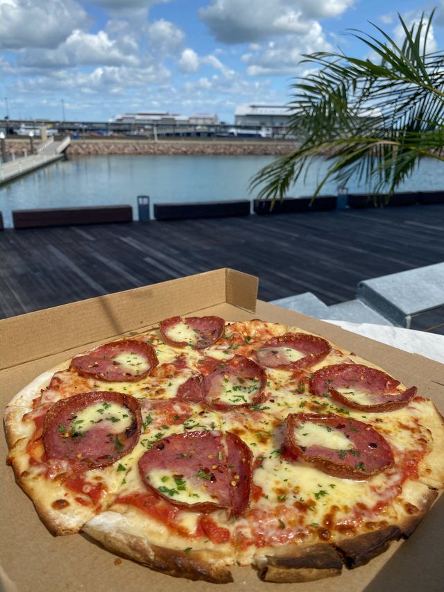 Pizza with pepperoni on a rooftop. Blue sky and palm tree in the background.