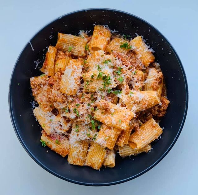 Rigatoni pasta with meat sauce and parmesan cheese in a black bowl.