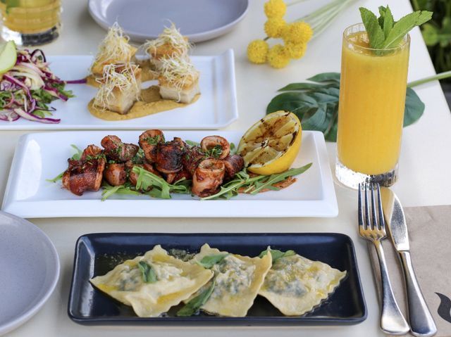 Table with plates of food and a drink. Includes pasta, fish, calamari, salad, and a yellow drink.