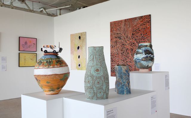 Art gallery with ceramic vases on pedestals, paintings on white walls.
