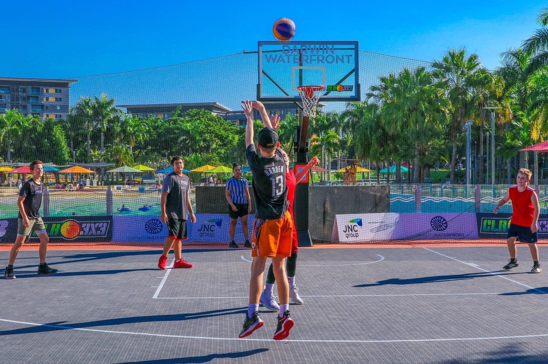 People playing basketball on an outdoor court under a sunny sky.