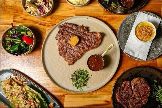 Overhead shot of a table with steak, sauce, salads, and creme brulee dishes.