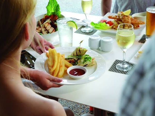 Person serving plate of food with fries and sauce at a table with other dishes and drinks.