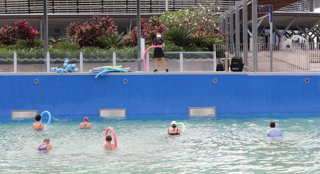 People swim in a wave pool, while a person stands on the pool's edge, holding a hula hoop.