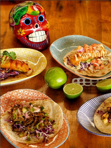 Colorful tacos on patterned plates with lime and skull decoration.