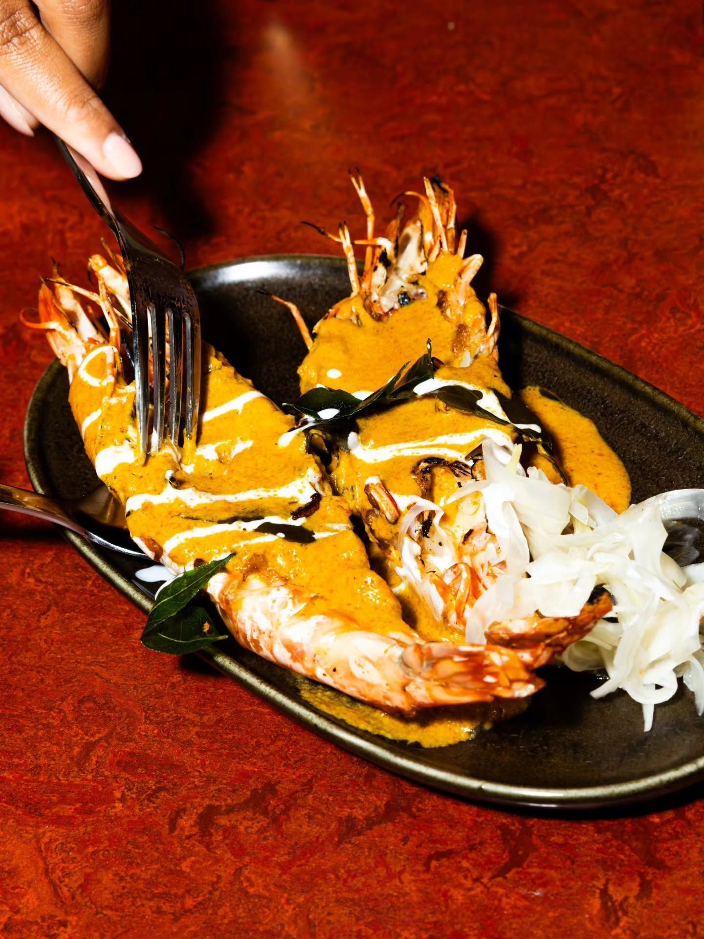 Person serving plate of food with fries and sauce at a table with other dishes and drinks.