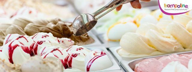 Ice cream scoops in a display. A hand holds a scoop. Many flavors with colorful toppings.