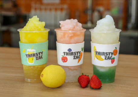 Three colorful slushies in cups with fruit and a 
