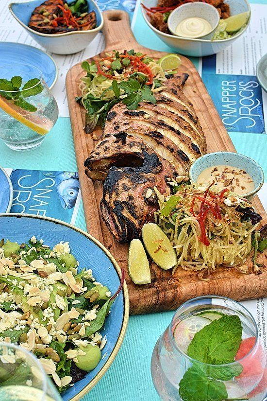 Grilled seafood platter with sides on a wooden board, set on a blue-themed table.