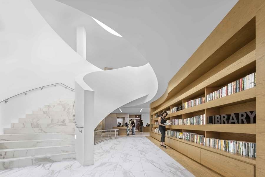 A woman is standing in a library next to a spiral staircase.