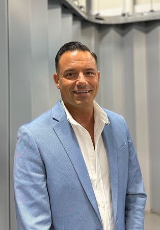 A man wearing a blue suit and a red lanyard is smiling for the camera.