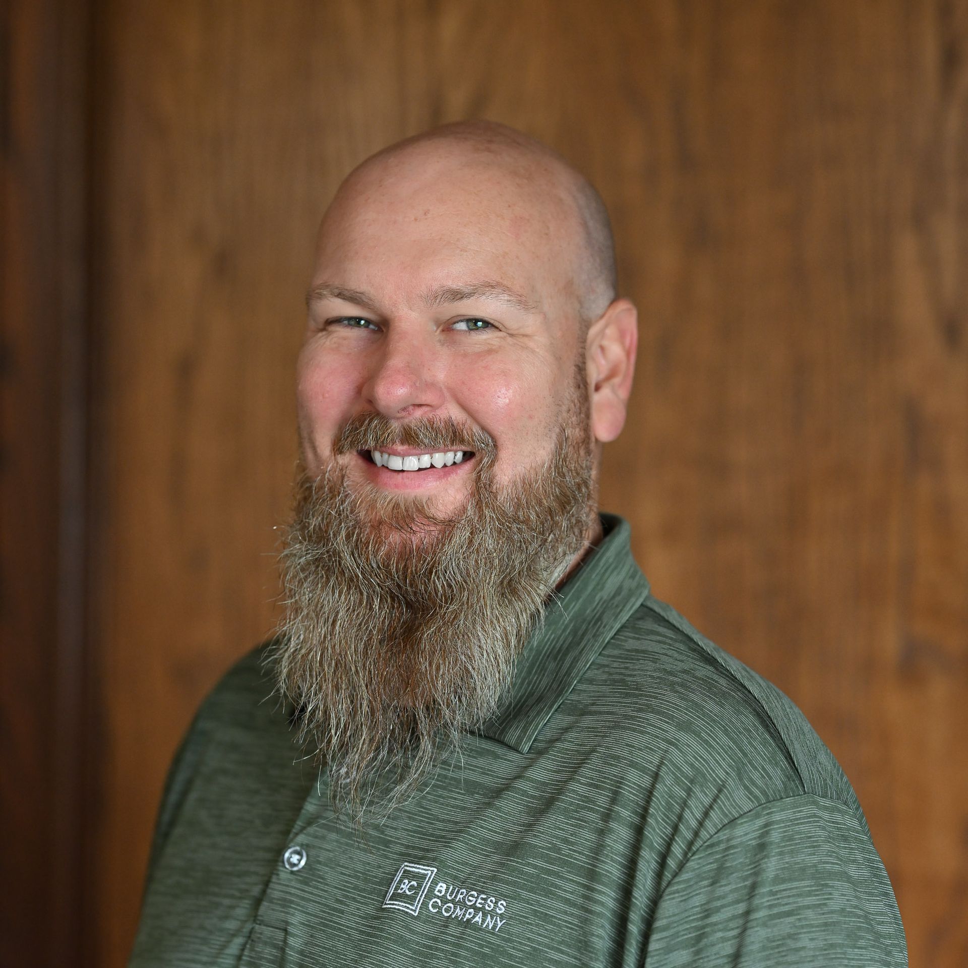 A man with a beard is wearing a green shirt and smiling.