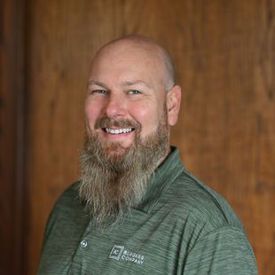 A man with a beard is wearing a green shirt and smiling.