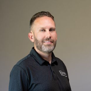 A man with a beard is wearing a black polo shirt and smiling for the camera.