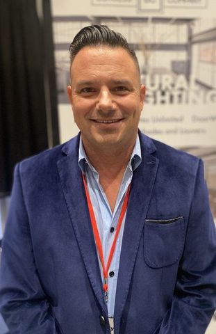 A man wearing a blue suit and a red lanyard is smiling for the camera.