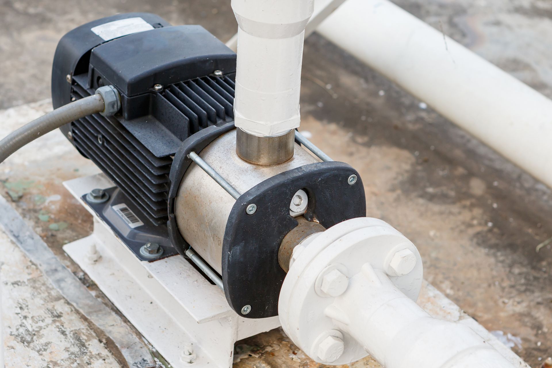 Electric water pump connected to white PVC pipes on a concrete floor.