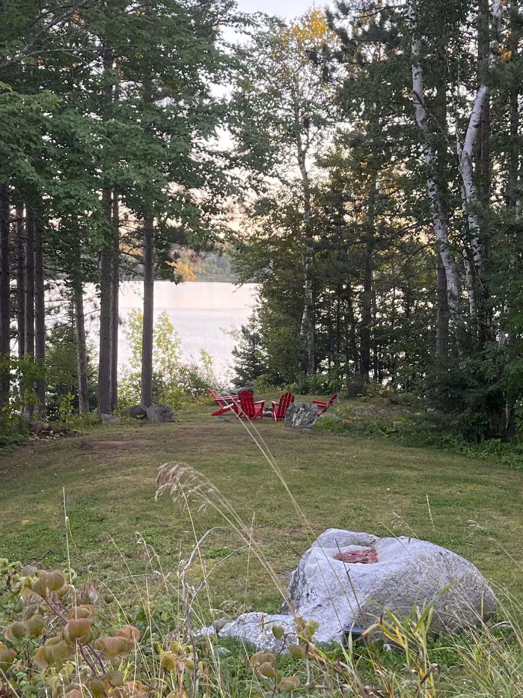 A fire pit in the middle of a grassy field with a lake in the background.