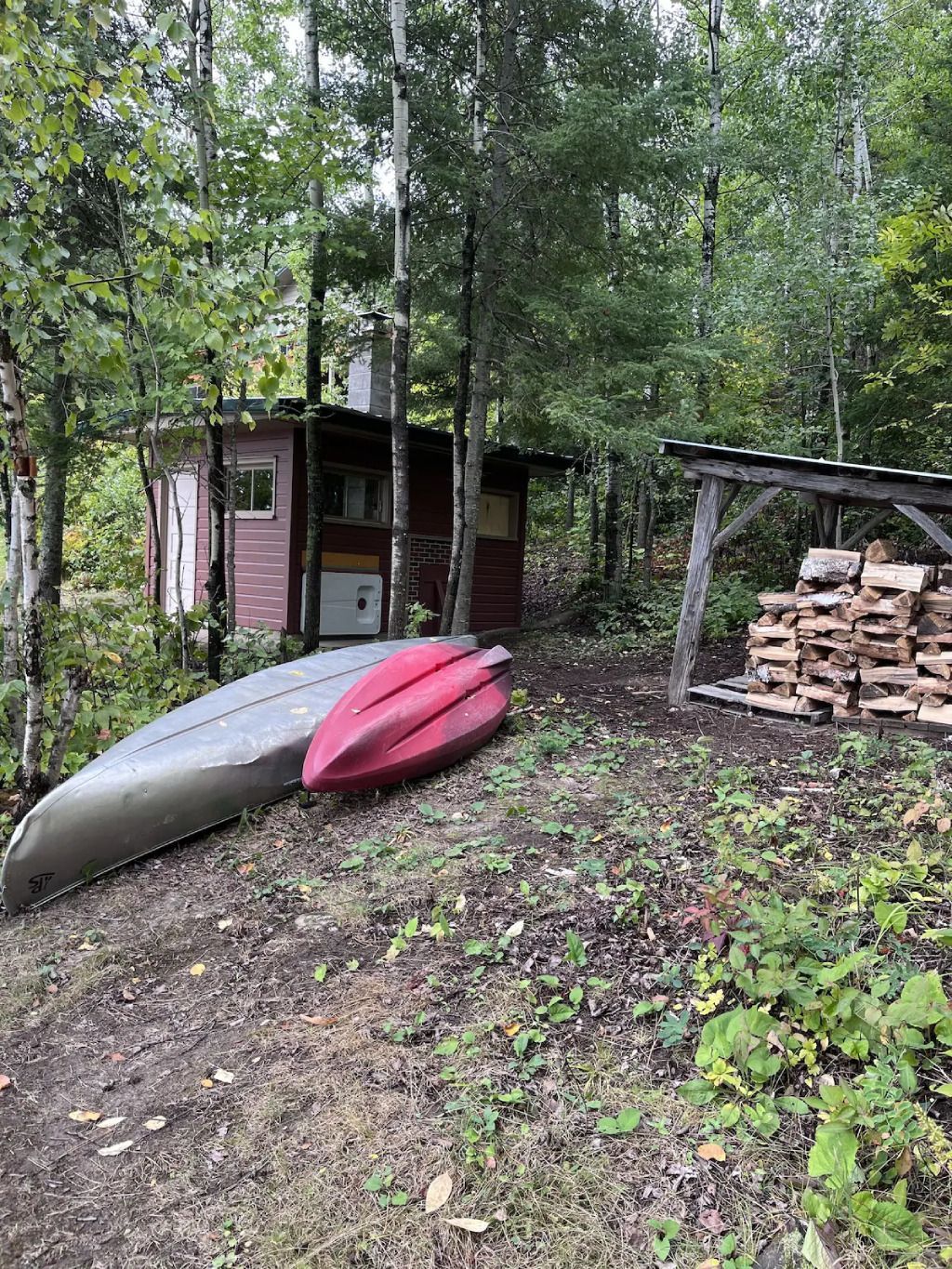 Two canoes are sitting on the ground next to a pile of wood.