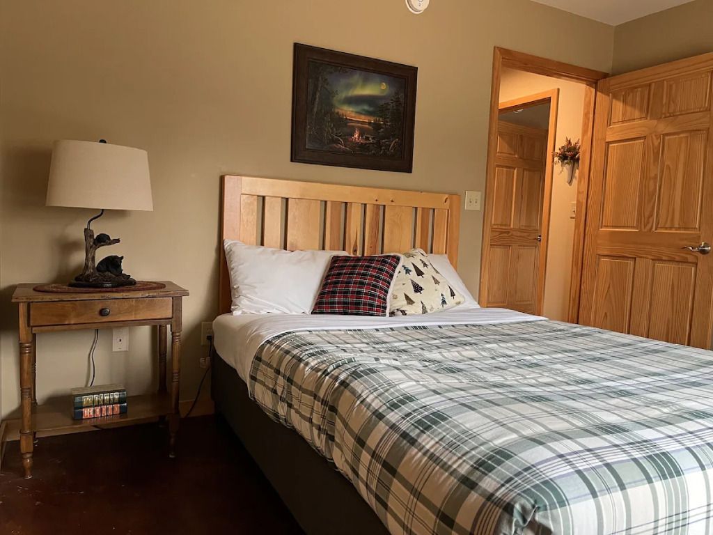 A bedroom with a bed , nightstand , lamp and painting on the wall.