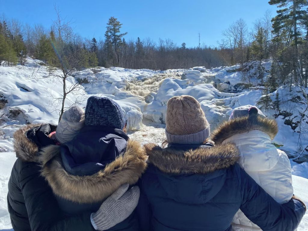 Three people are standing in the snow looking at a waterfall.