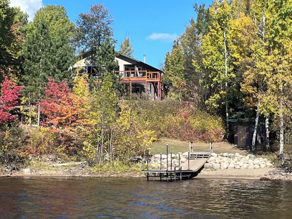A house is sitting on top of a hill next to a lake surrounded by trees.