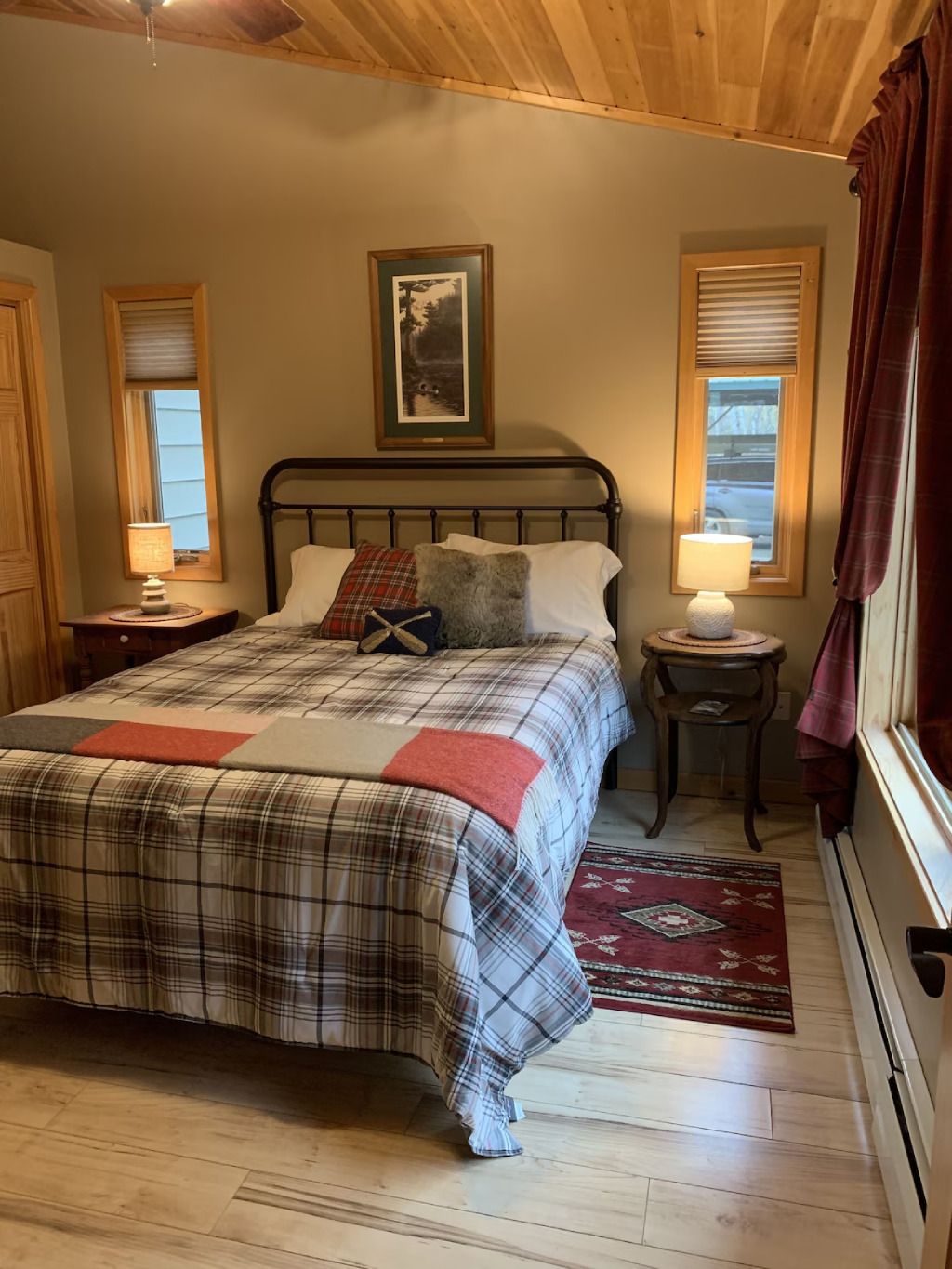 A bedroom with a bed , two nightstands , two windows and a rug.