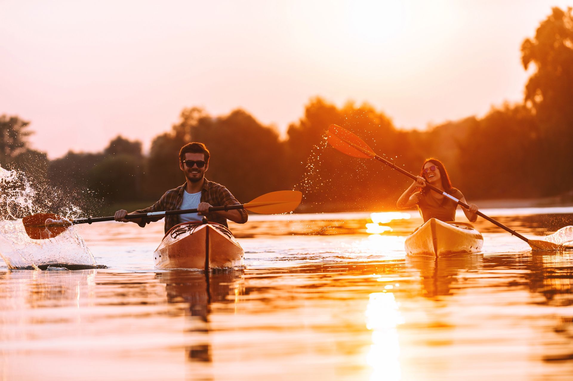 A man and a woman are paddling kayaks on a river at sunset.