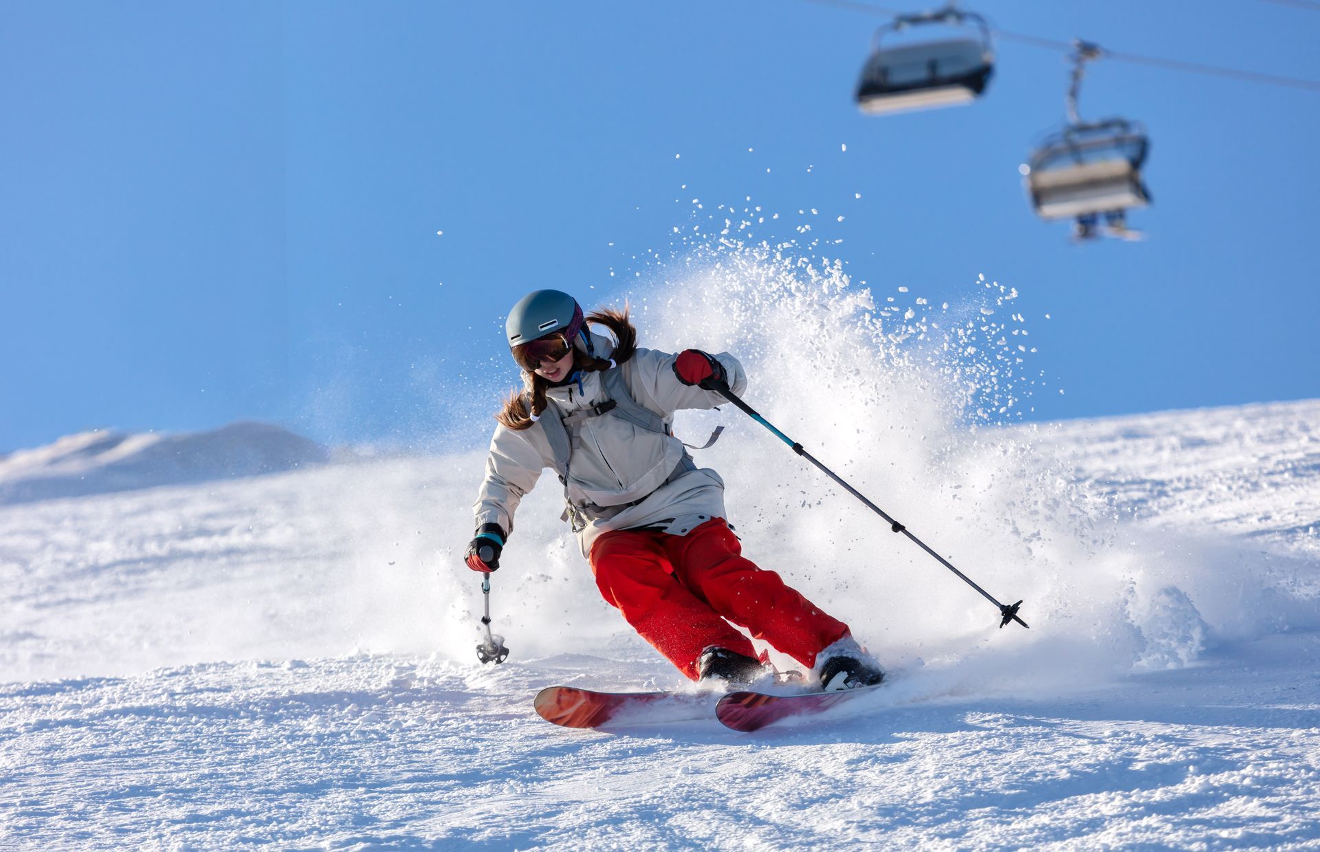 A woman is skiing down a snow covered slope with a ski lift in the background.